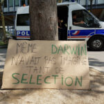 Pancarte avec slogan devant l'université Pierre et Marie Curie place Jussieu paris, sur la pancarte: « Même Darwin n'avait pas imaginé tant de selection». Un camion de police est présent entre la pancarte et l'université.